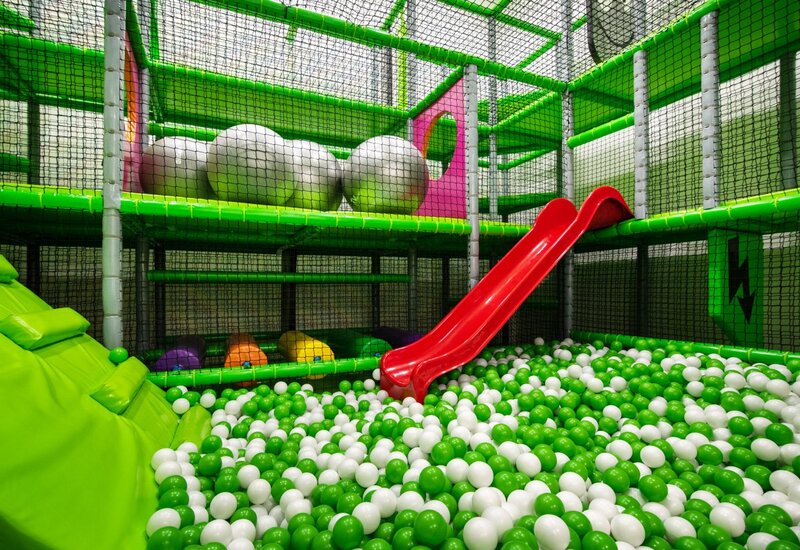 Indoor-Spielbereich für Kinder mit grün-weißem Bällebad, roter Rutsche, gepolsterten Plattformen und netzgeschütztem mehrstöckigem Spielgerüst