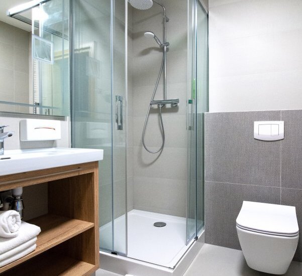 Modernes Hotelbadezimmer mit Glasdusche und Regenbrause, Holzwaschtisch mit frischen Handtüchern und wandhängendem WC