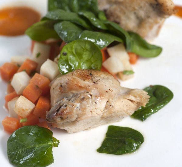 Gourmet-Teller mit gebratenem Geflügel, gewürfeltem Wurzelgemüse, frischem Babyspinat und Sauce‑Pünktchen auf weißem Teller