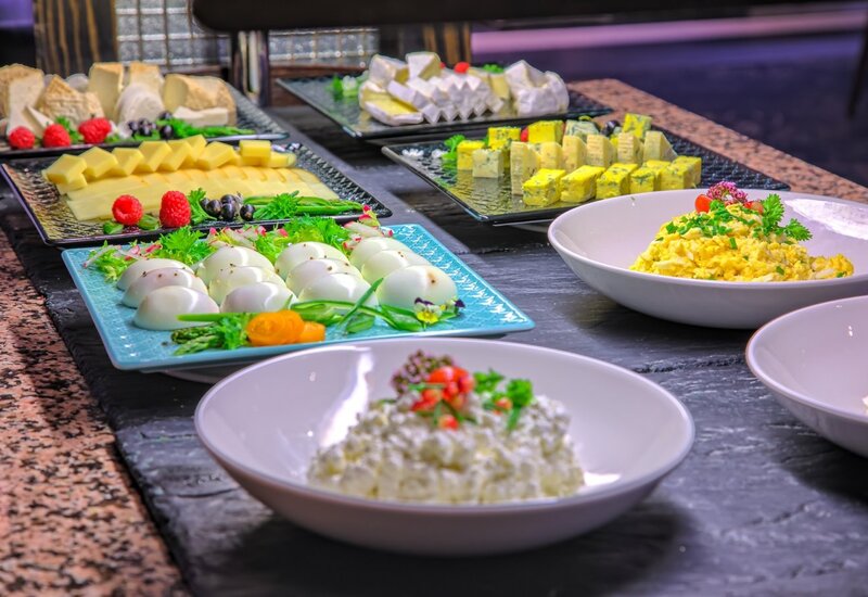 Frühstücksbuffet mit Käseplatten, gekochten Eiern, Rührei und mit Kräutern garniertem Hüttenkäse.