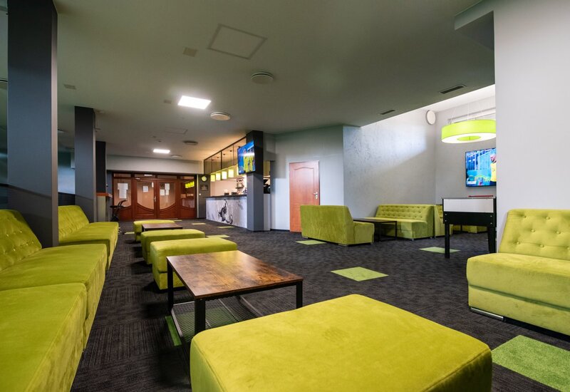 Moderne Hotellounge mit limonengrünen Sofas und Hockern, niedrigen Holztischen, TV, Kickertisch und Bar