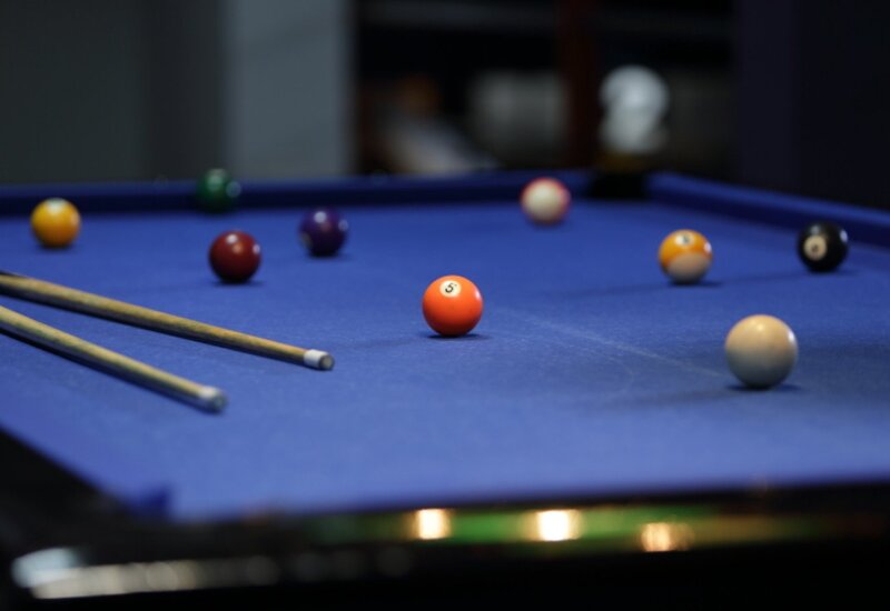 Spielzimmer mit blauem Billardtisch, zwei Queues und verstreuten Kugeln, ideal für gesellige Spielrunden
