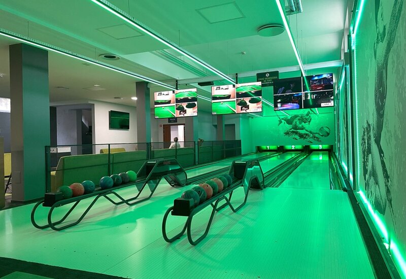 Zwei Bowlingbahnen mit grünem LED-Licht, Kugelablagen, Anzeigemonitoren und Lounge-Sitzbereichen