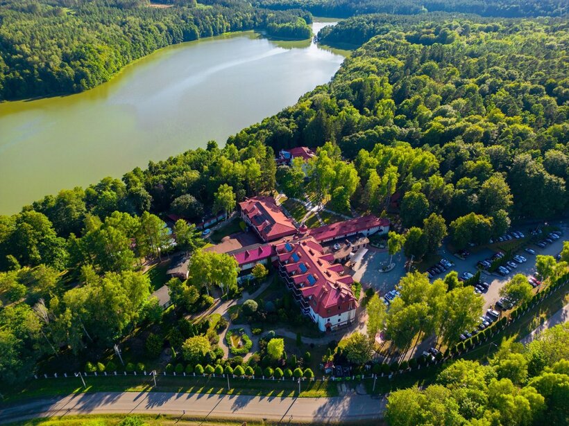 Seeresort mit roten Dächern, gepflegten Gärten, Parkplätzen und Waldwegen am ruhigen See, umgeben von dichtem Grün