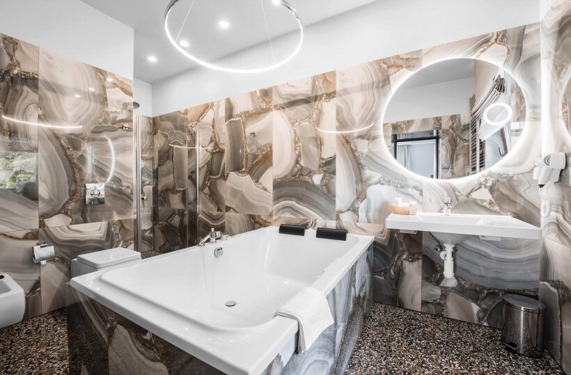 Luksusowa łazienka hotelowa z głęboką wanną, marmurowymi panelami, podświetlanym okrągłym lustrem i kabiną prysznicową