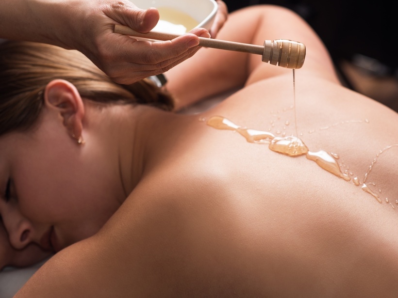 Gast liegt mit dem Gesicht nach unten bei Honig-Rückenmassage, Therapeut gießt warmes Öl mit Holzlöffel im Spa.