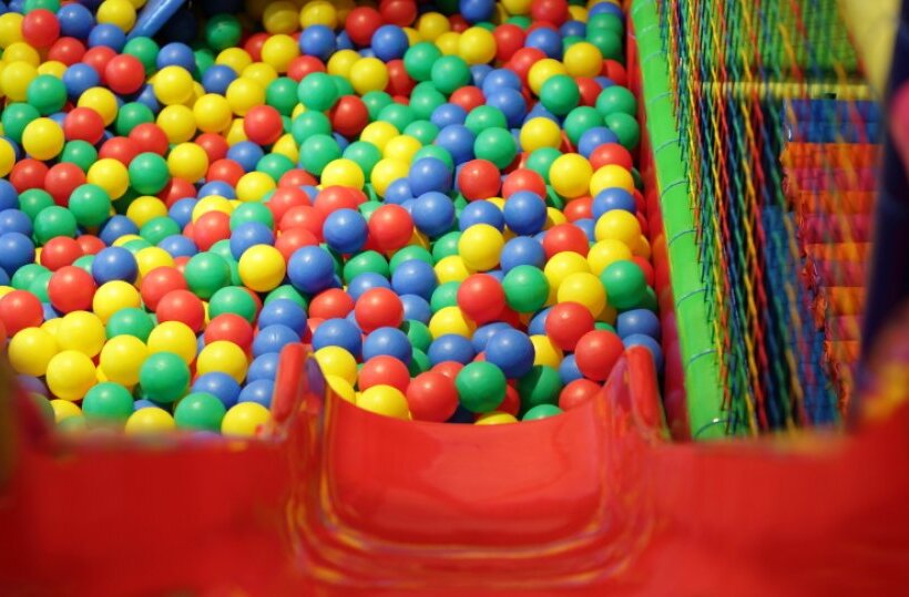 Colorful indoor kids' play area with red slide into a multicolored ball pit and safety netting