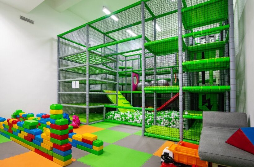 Indoor kids' play area with multi-level soft play structure, ball pit, slides, colorful foam blocks and seating.