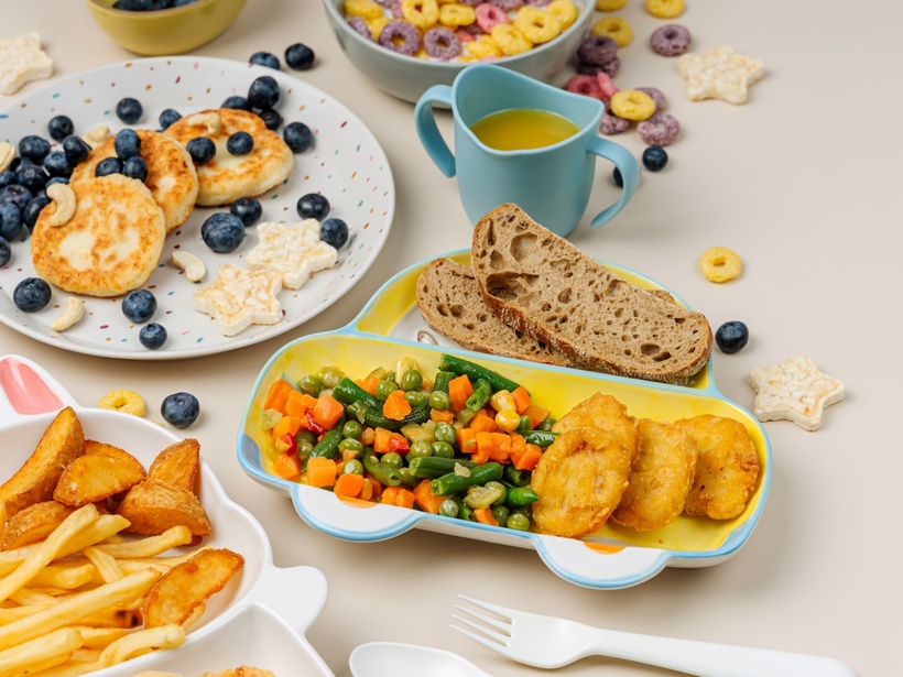 Child-friendly plated meal: nuggets, mixed vegetables, rye bread, fries, blueberry pancakes and a cup of juice