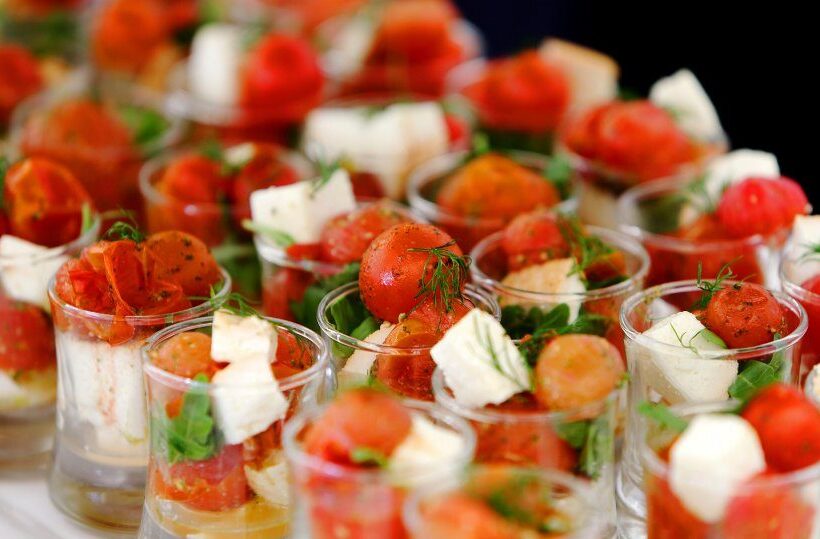 Individual caprese appetizers in clear cups with cherry tomatoes, mozzarella and fresh herbs, perfect for receptions or buffets