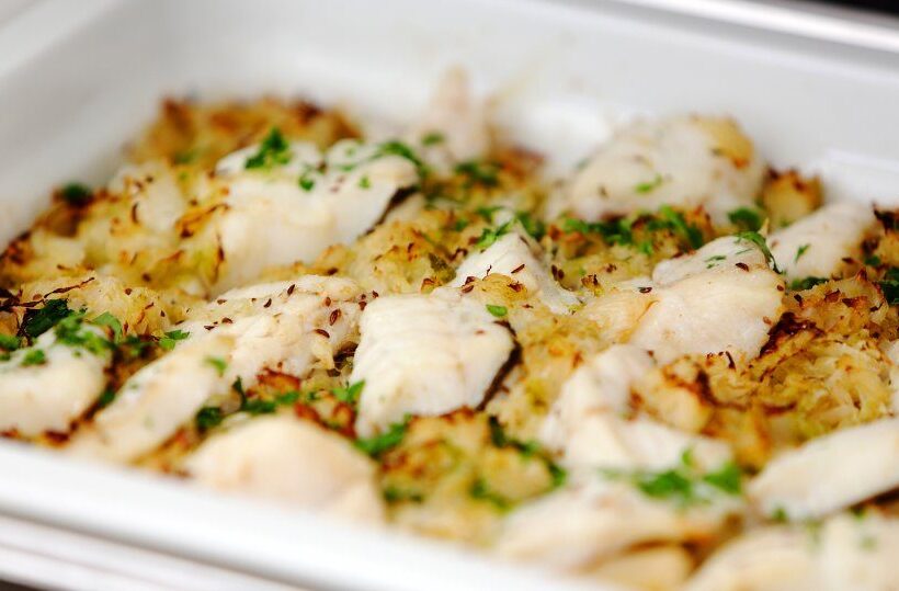 Baked white fish fillets on herbed breadcrumb and rice bed, garnished with parsley, in a stainless buffet tray