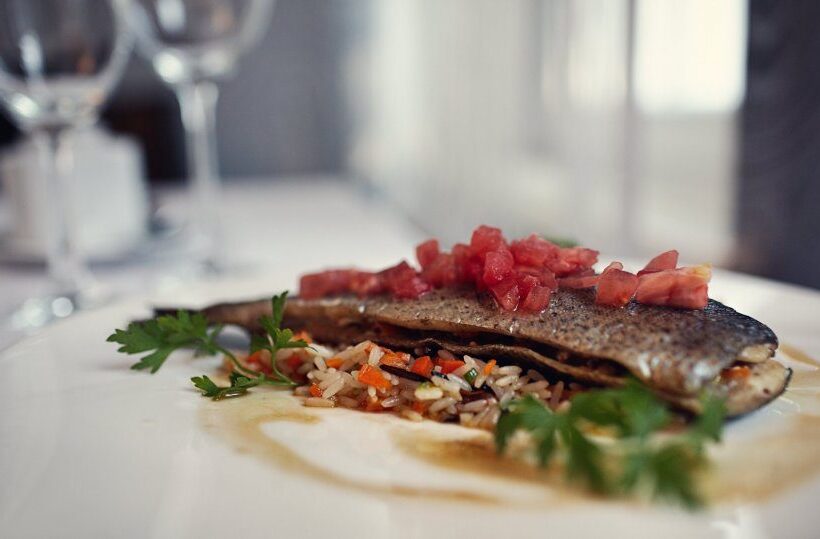Gebratener Fisch auf gewürztem Reis mit Tomatenwürfeln und Petersilie, auf weißem Tischtuch serviert in einem eleganten Restaurant.