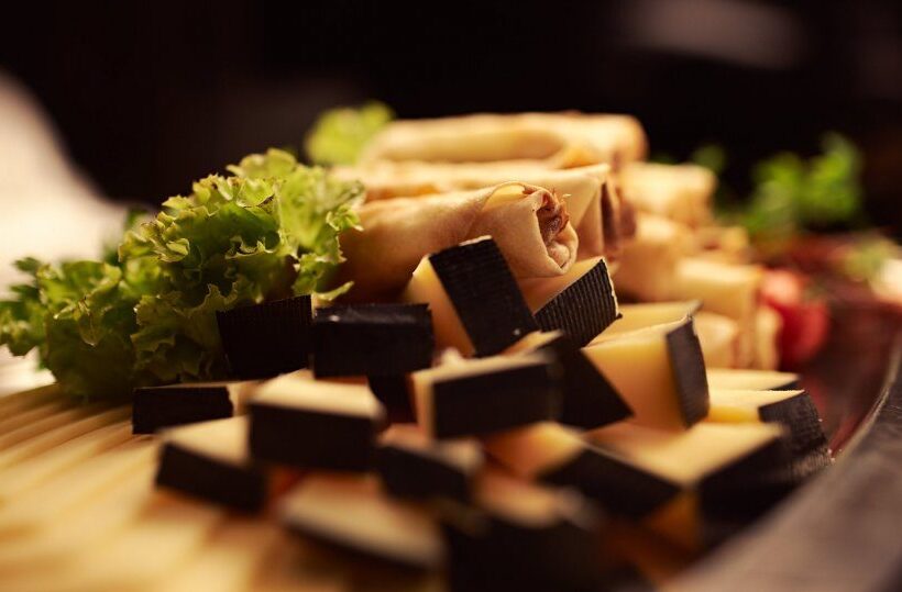 Vorspeisenplatte: gestapelte Frühlingsrollen, Käsewürfel mit dunklem Rand und Salatgarnitur