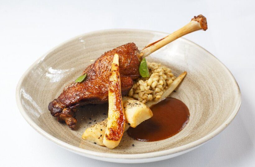 Knusprige Entenkeule auf Gerstenrisotto mit glasiertem Wurzelgemüse und reichhaltiger Demi-Glace, serviert in einer eleganten Keramikschale