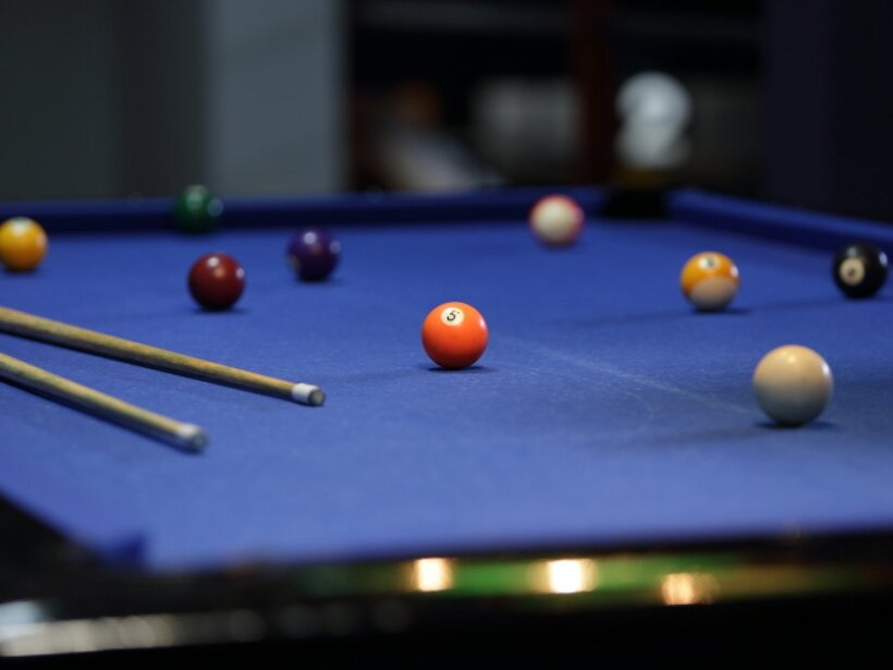 Spielzimmer mit blauem Billardtisch, zwei Queues und verstreuten Kugeln, ideal für gesellige Spielrunden