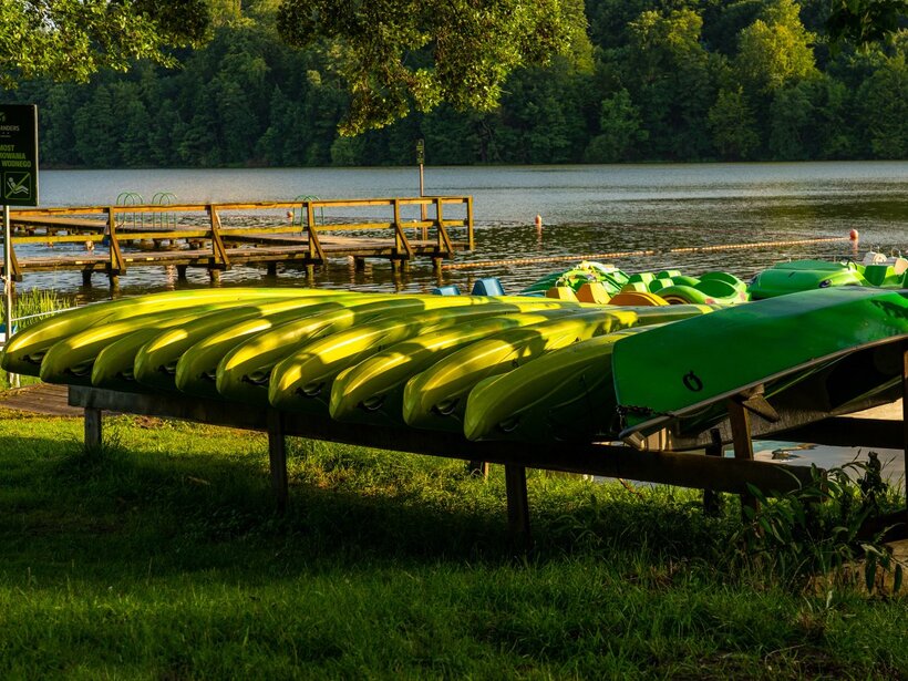 Bright lime kayaks stacked on a rack beside a wooden hotel dock overlooking a calm lake and forest at golden hour