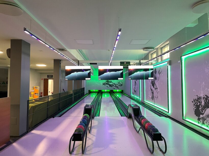 Moderne Bowlingbahn mit drei Bahnen, grünem Neonlicht, Anzeigemonitoren über den Bahnen und Kugelständern