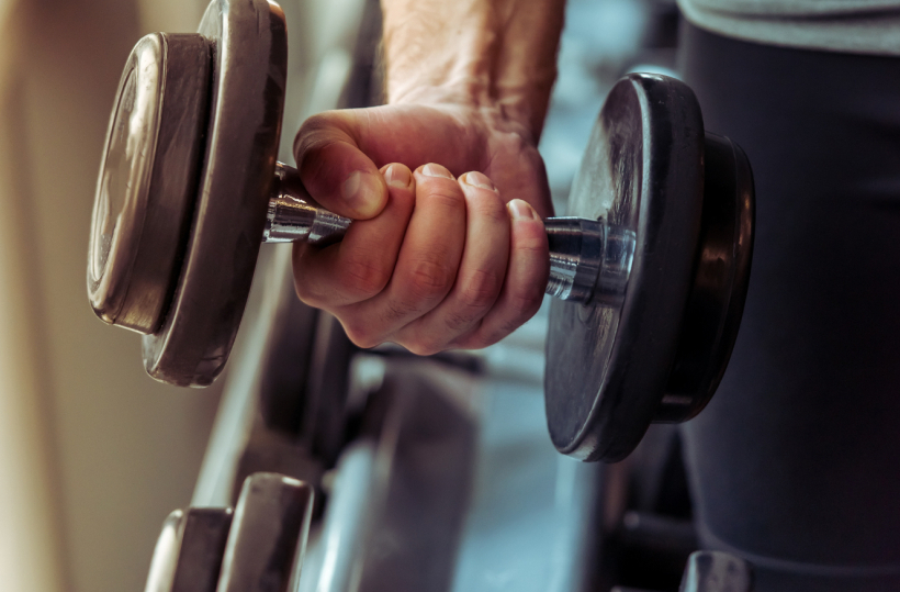 Guest hand gripping a dumbbell in the hotel fitness center, close-up of free weights and training area