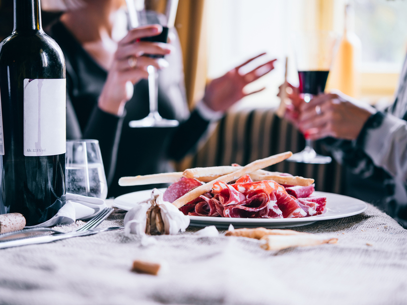 Bottle of wine and charcuterie plate with breadsticks on a rustic table as two guests toast with glasses