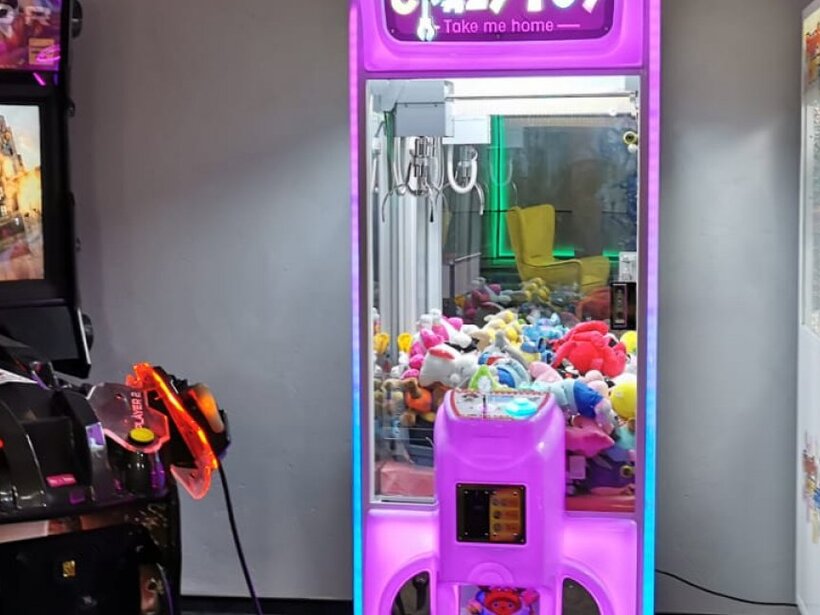 Neonbeleuchtete Spielzone im Hotel mit Greifautomaten voller Kuscheltiere und einem Shooter-Automaten für Familien