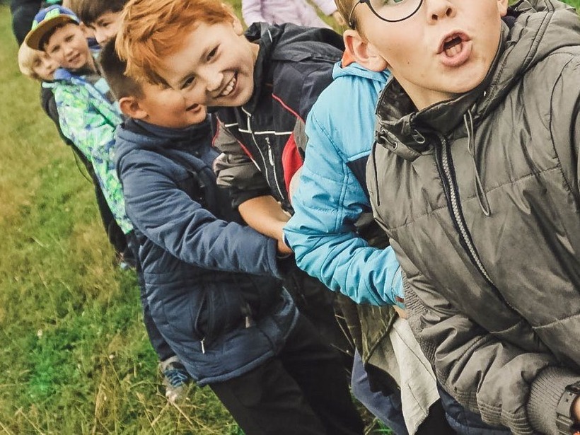 Kinder in Jacken lachen, während sie auf einer Wiese bei einem Tauziehen an einem Seil ziehen
