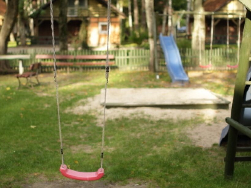 Familienfreundlicher Außenbereich mit rosa Schaukel, Holzklettergerüst, blauer Rutsche, Sandkasten und Parkbänken