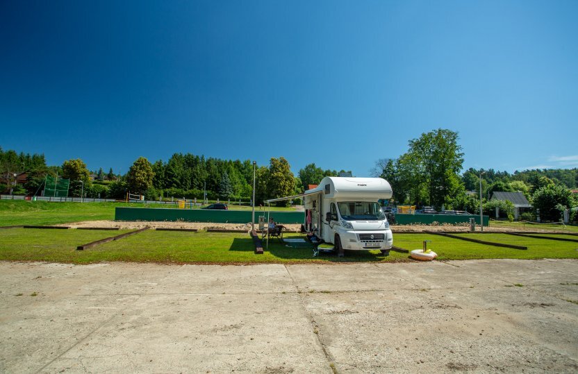 Wohnmobil auf grüner Campingparzelle mit Markise und Außenstühlen, sonniger Himmel, baumbestandene Anlage, ruhiger Aufenthalt