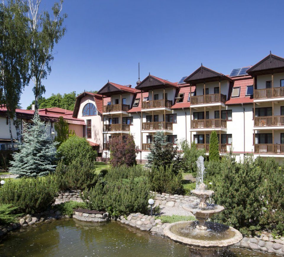 Hotel im villenähnlichen Stil mit roten Dächern und Holzbalkonen, gepflegten Gärten, Wegen und Springbrunnen am Teich