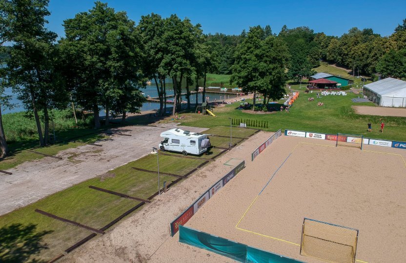 Seenahe Anlage: Sand-Volleyballfeld, Camper-Stellplatz, Rasen-Picknickbereich, schattiger Steg und Badende