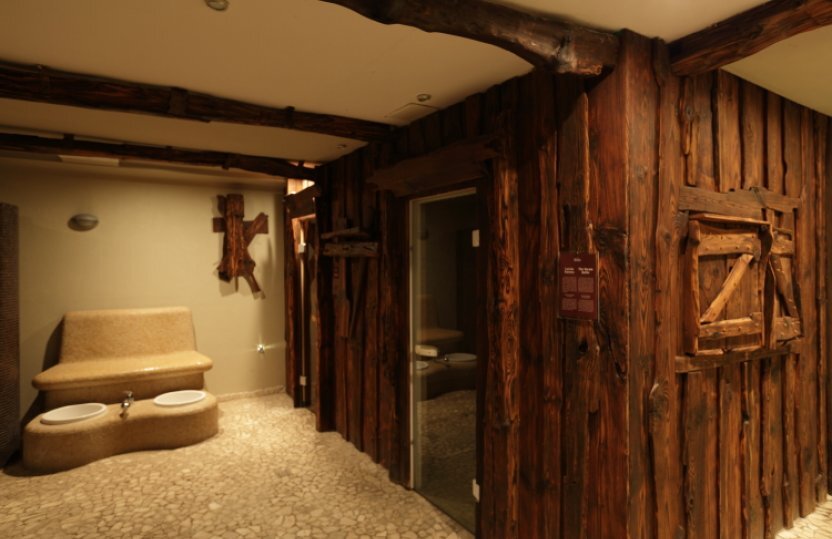 Rustikaler Spa-Bereich mit zwei Fußbädern, Kiesboden, holzverkleideten Wänden und Glastür zur Sauna