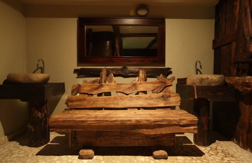 Rustikale, geschnitzte Holzbank mit Konsole und Steinwaschbecken, warmes Spa‑Ambiente