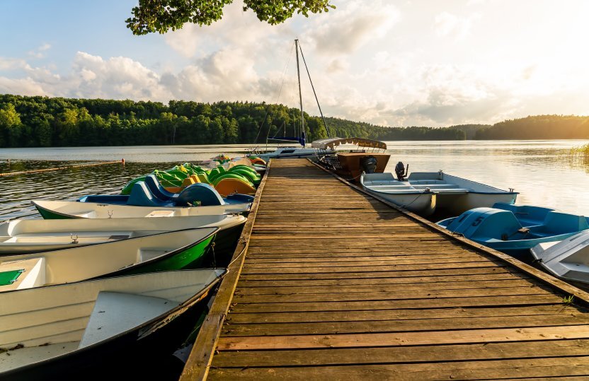 Wooden hotel pier with rental rowboats and pedal boats on a calm lake, forested shoreline and sunset glow.