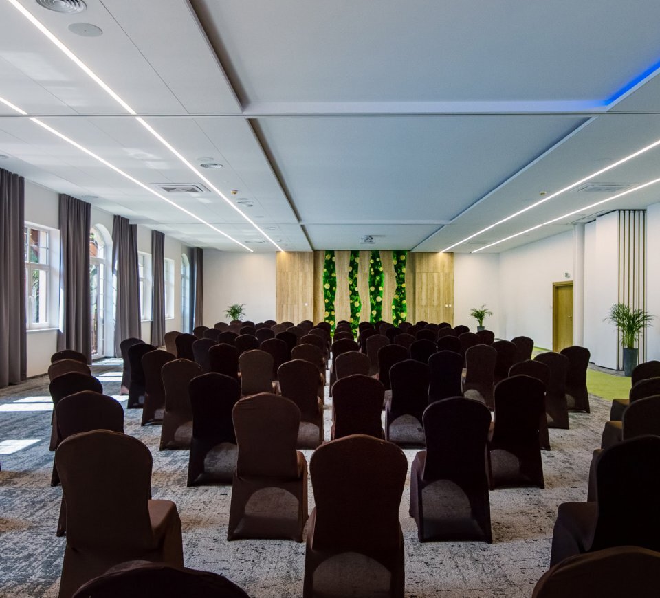 Spacious modern conference room with rows of covered chairs, large windows, green living wall and ceiling projector