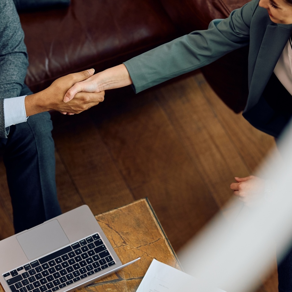 Handshake between professionals in a hotel lounge, leather sofa and wooden table with laptop and smartphone
