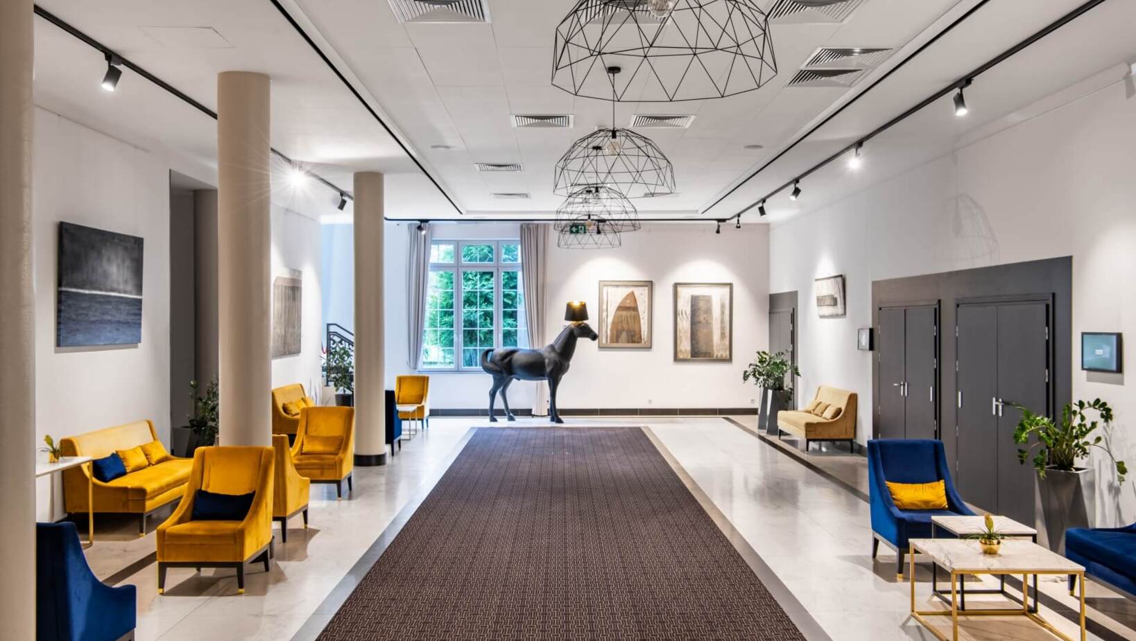 Industrialny korytarz hotelowy, z eleganckimi fotelami przestronnie urządzony oraz rzeźba