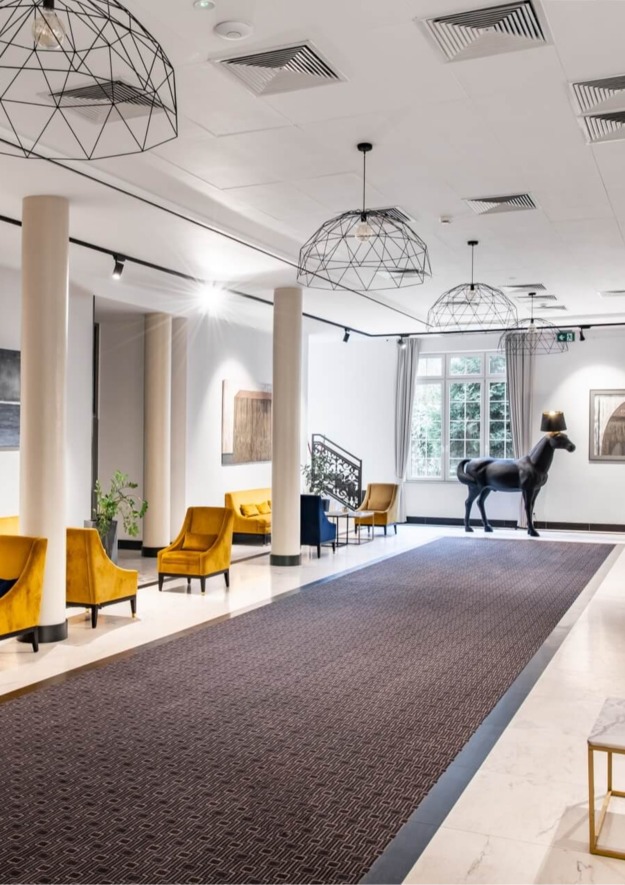 Korytarz hotelowy z jasnym oświetleniem, eleganckimi pomarańczowymi fotelami i rzeźbą