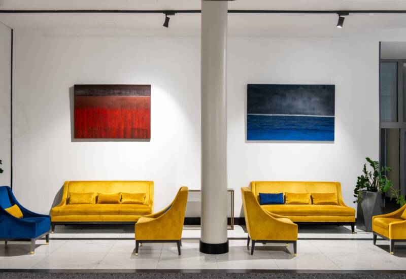 Korytarz hotelowy z wygodnymi kolorowymi sofami oraz fotelami, na ścianie fantazyjne obrazy