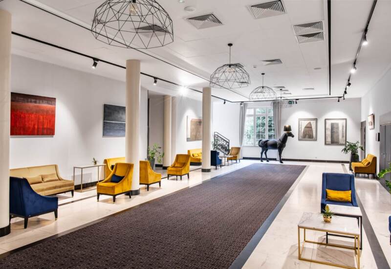 Korytarz hotelowy z jasnym oświetleniem, eleganckimi pomarańczowymi fotelami i rzeźbą