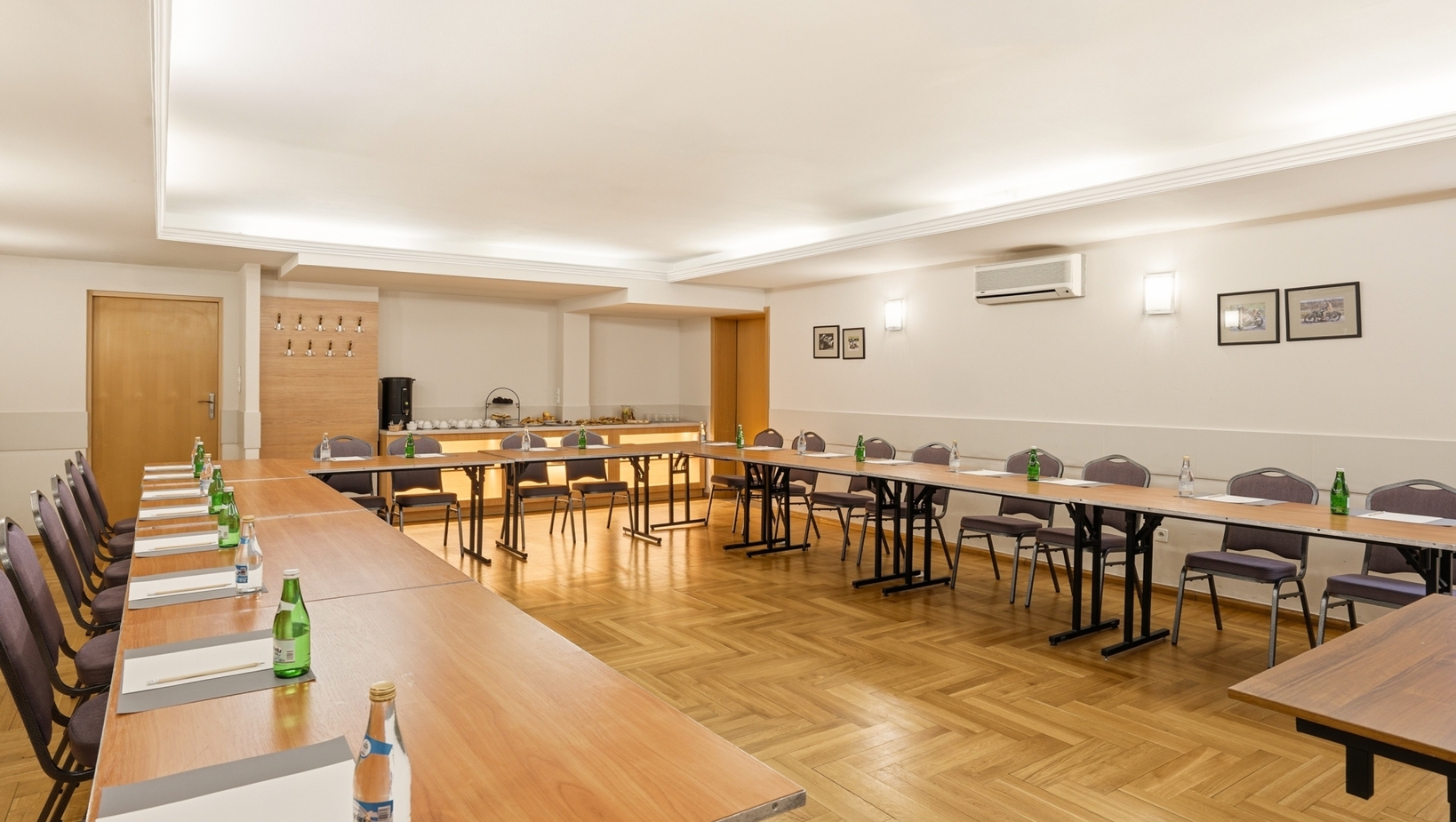 Sala konferencyjna w układzie U z drewnianymi stołami, krzesłami, butelkowaną wodą, notesami i stacją kawową