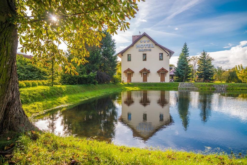 Trzygwiazdkowy hotel wiejski przy spokojnym stawie, z nasłonecznionym trawnikiem i drzewami, idealny na relaks nad wodą.