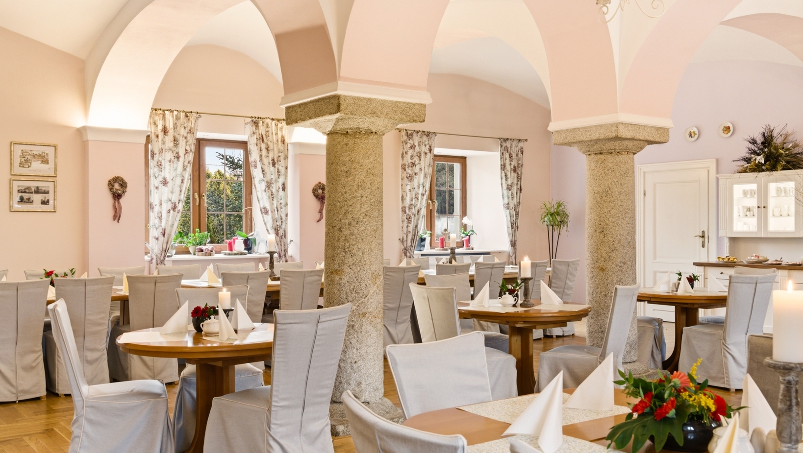 Elegancka sala restauracyjna z jasnoróżowymi sklepieniami, surowymi kamiennymi filarami i drewnianymi stołami nakrytymi świecami i kwiatami