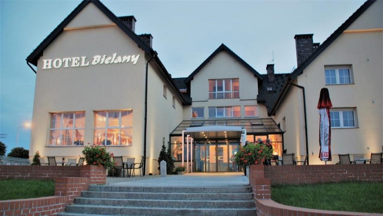 Fasada Hotelu Bielany o zmierzchu z przeszklonym wejściem, ciepło oświetlonymi oknami, tarasem i ceglanymi schodami