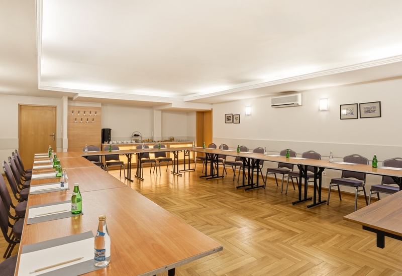 Sala konferencyjna w układzie U z drewnianymi stołami, krzesłami, butelkowaną wodą, notesami i stacją kawową