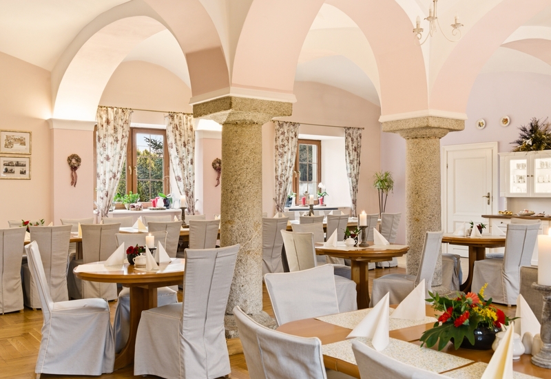 Elegancka sala restauracyjna z jasnoróżowymi sklepieniami, surowymi kamiennymi filarami i drewnianymi stołami nakrytymi świecami i kwiatami