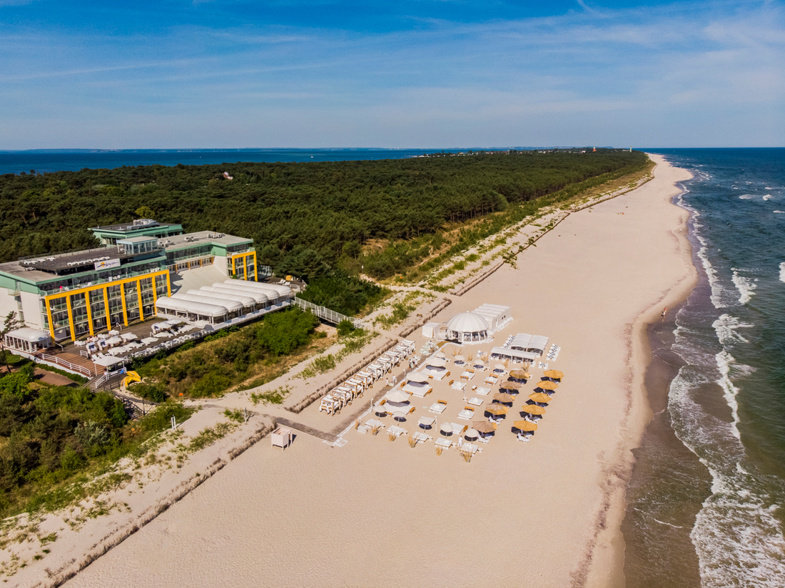 Nadmorski ośrodek: nowoczesny hotel z żółtymi akcentami, taras, plażowy klub z pawilonami, leżakami i parasolami