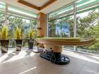 Sunlit spa treatment room with modern massage table, hanging oil bowl, floor-to-ceiling windows and tall planters overlooking pine forest.