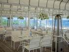 Tarasowa restauracja hotelowa z białymi stołami, wiszącymi koszami kwiatów, ogrzewaczami i widokiem na morze