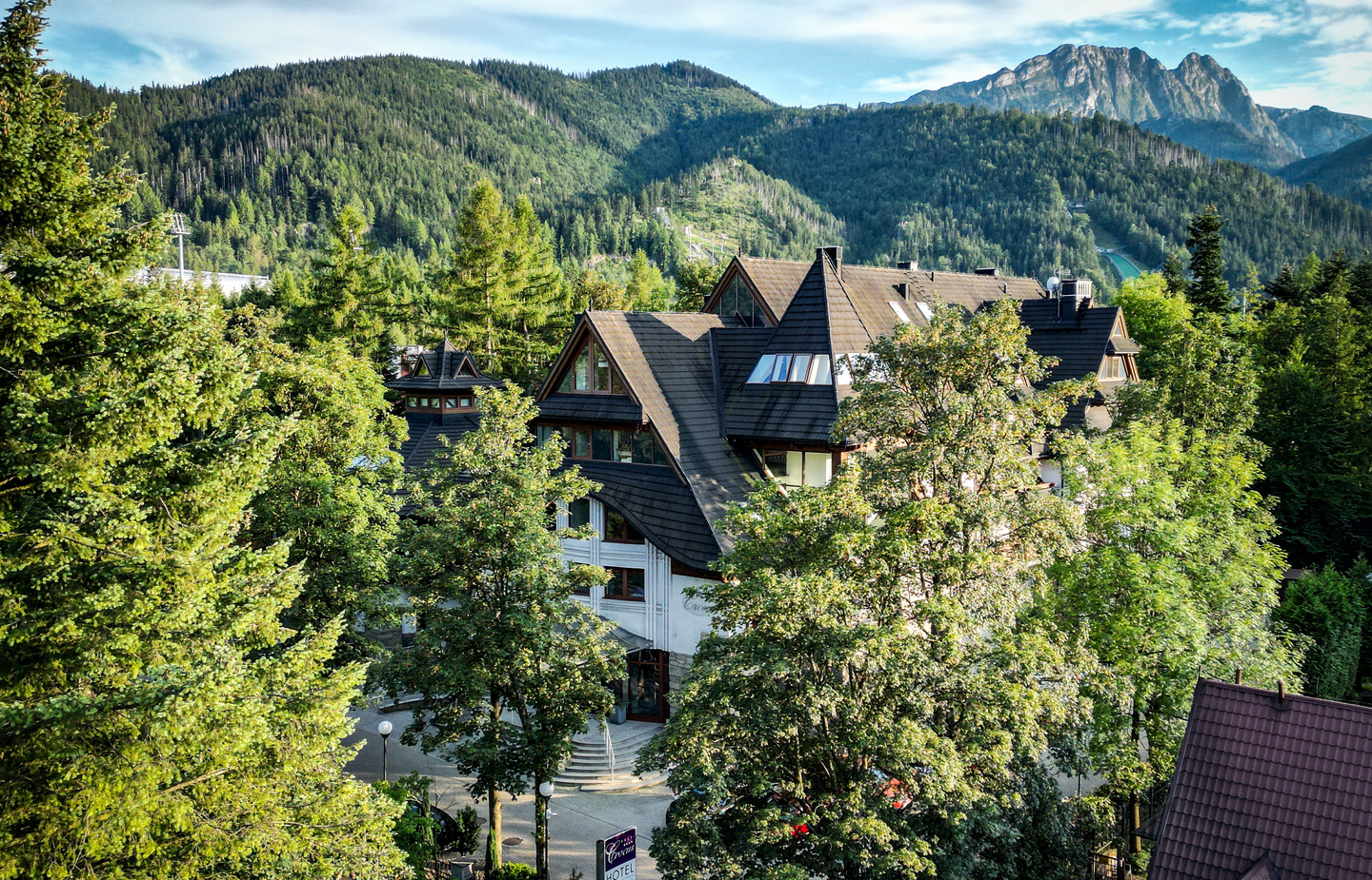 فندق جبلي بطراز شاليه بسقوف حادة ونوافذ علوية، محاط بأشجار الصنوبر مع إطلالة بانورامية على الجبال.