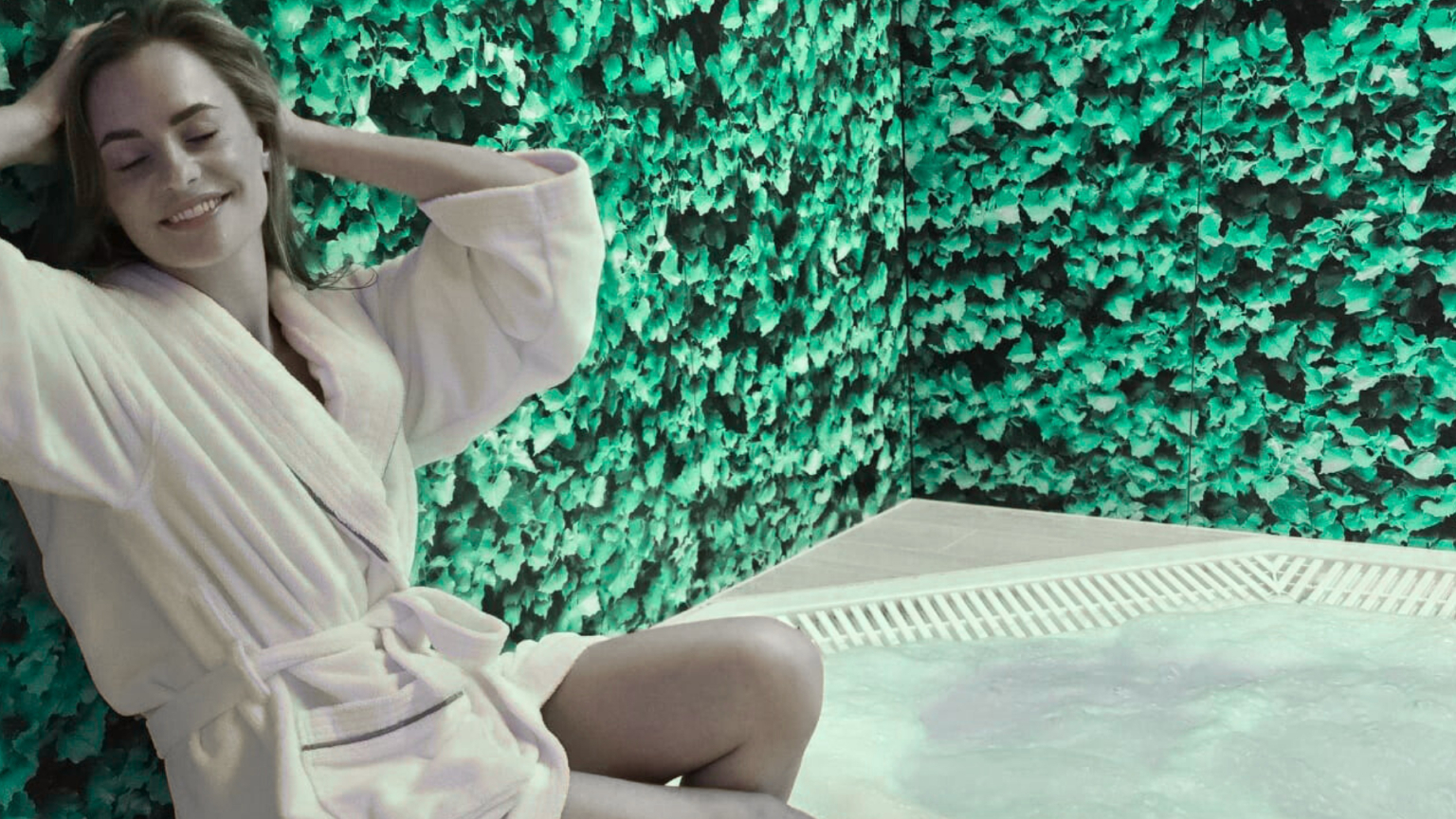 Žena v bielom župane relaxuje pri bublinkovej vírivke pred zelenou živou stenou v hotelovom spa