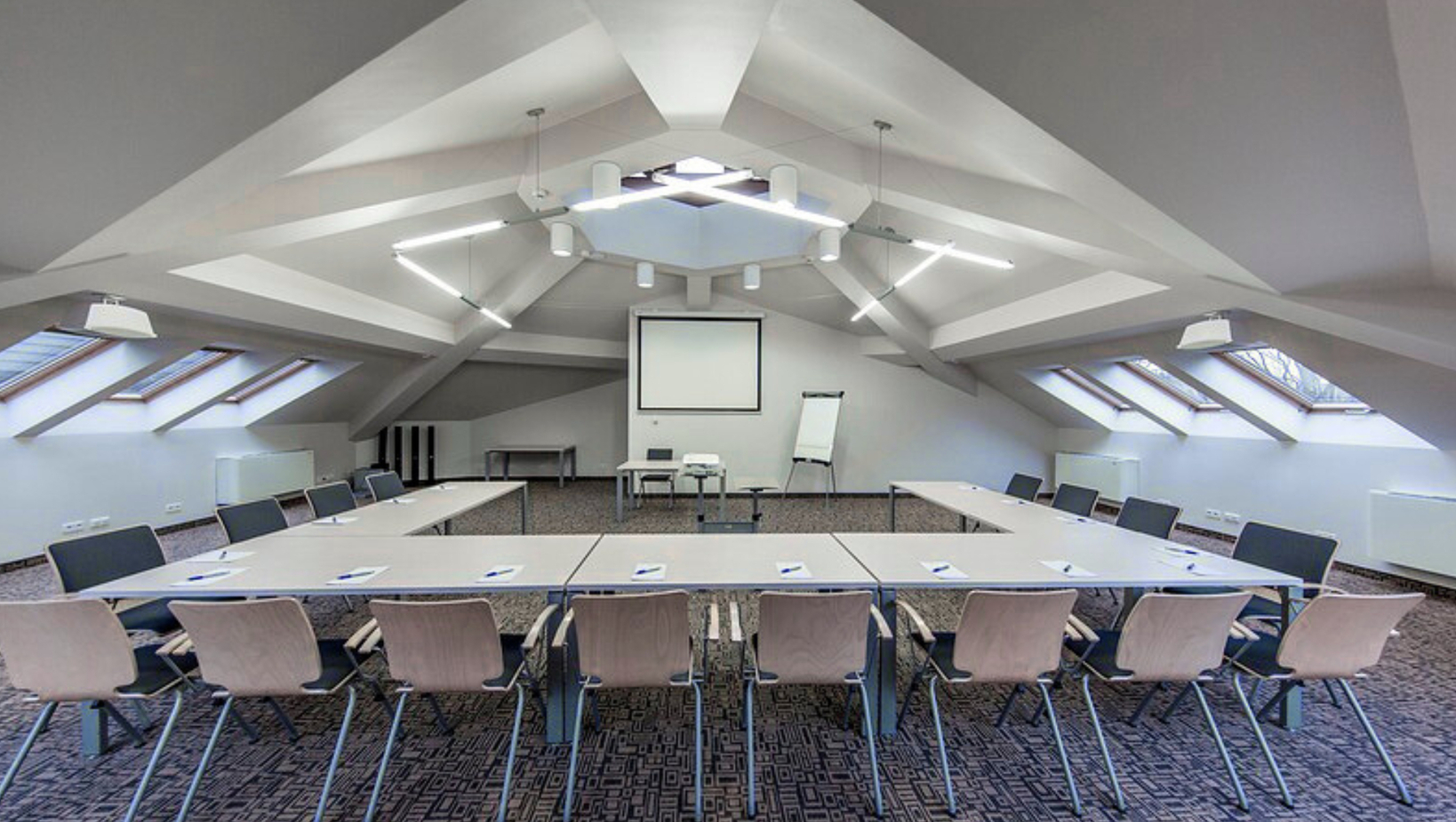 قاعة اجتماعات فندقية في العلية بترتيب طاولات على شكل U، شاشة عرض، سبورة متنقّلة، نوافذ سقفية وإضاءة عصرية